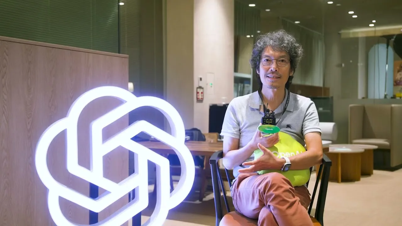 An event participant holding a microphone beside an illuminated OpenAI logo.