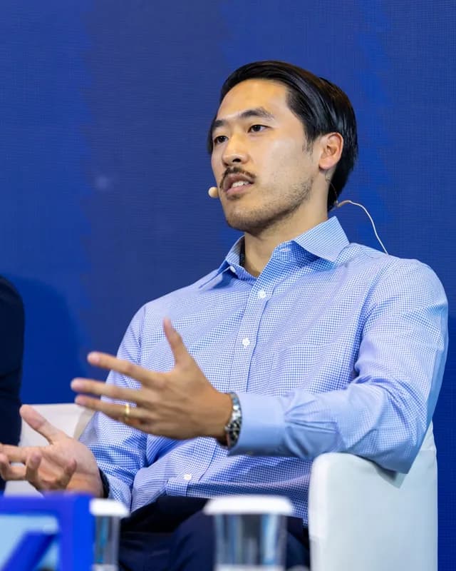 Derrick Choi gesturing during a seated panel discussion.